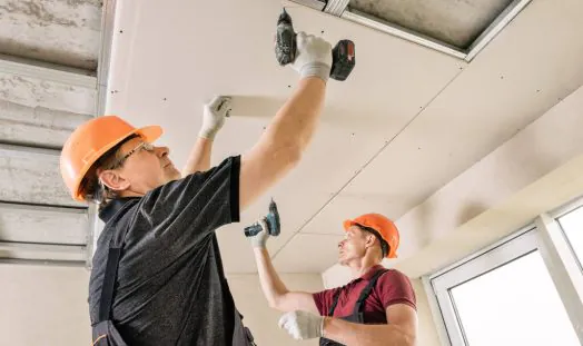 Installation of drywall. Workers are using screws and a screwdriver to attach plasterboard to the ceiling.